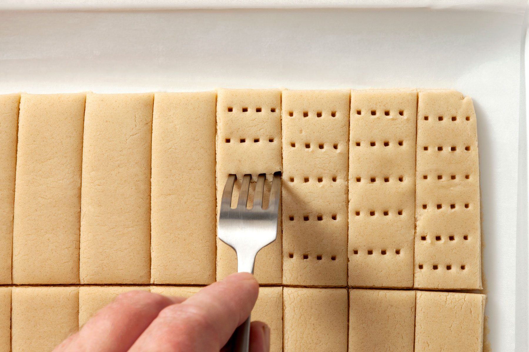 Strips of dough are being pricked by a fork.