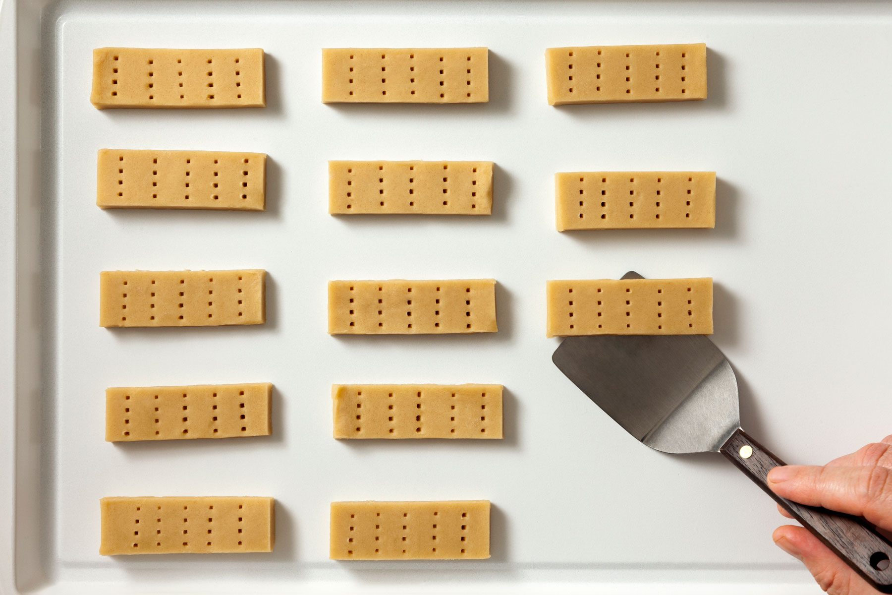 Cookies arranged 1 inch apart on an ungreased baking sheet. A hand holding a spatula is seen placing one of the cookies.