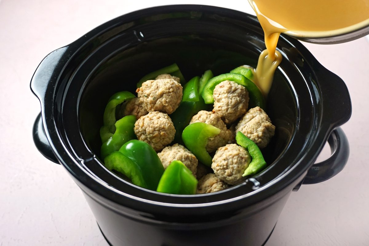 Pouring sauce over green peppers and meatballs in a crock pot to make slow cooker sweet and sour meatballs for Taste Recipes RMS 27421