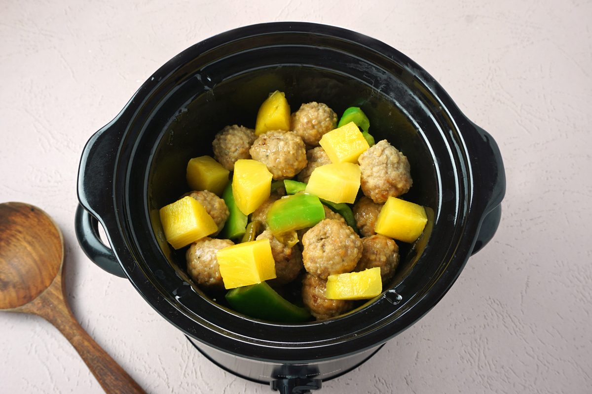 A crockpot with pineapple, green peppers, ad meatballs to make slow cooker sweet and sour meatballs for Taste Recipes RMS 27421