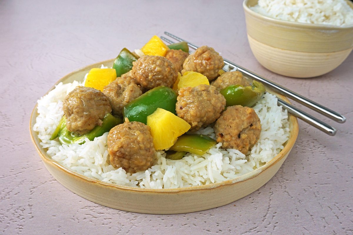 A plate of slow cooker sweet and sour meatballs with rice and chopsticks for Taste Recipes RMS 27421