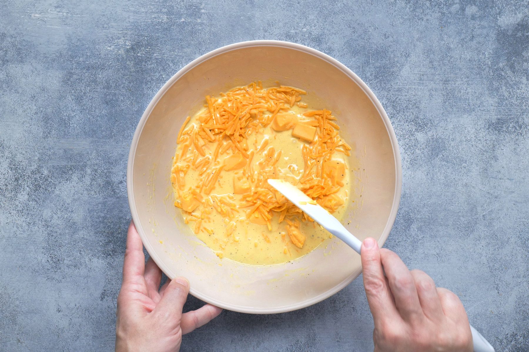 Velveeta and mild and sharp cheddar cheeses being added to sauce in a bowl.