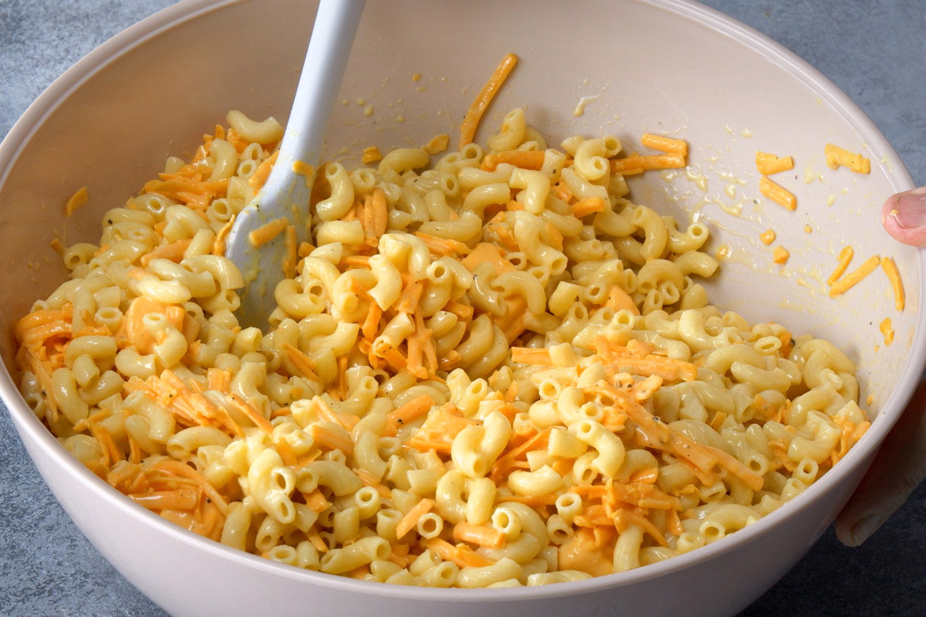 Macaroni and cheese mixture being combined in a large bowl.