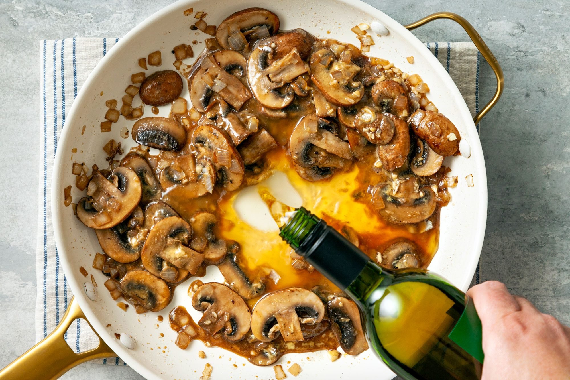 overhead shot; grey textured background; added wine to mushrooms in pan placed over kitchen towel;