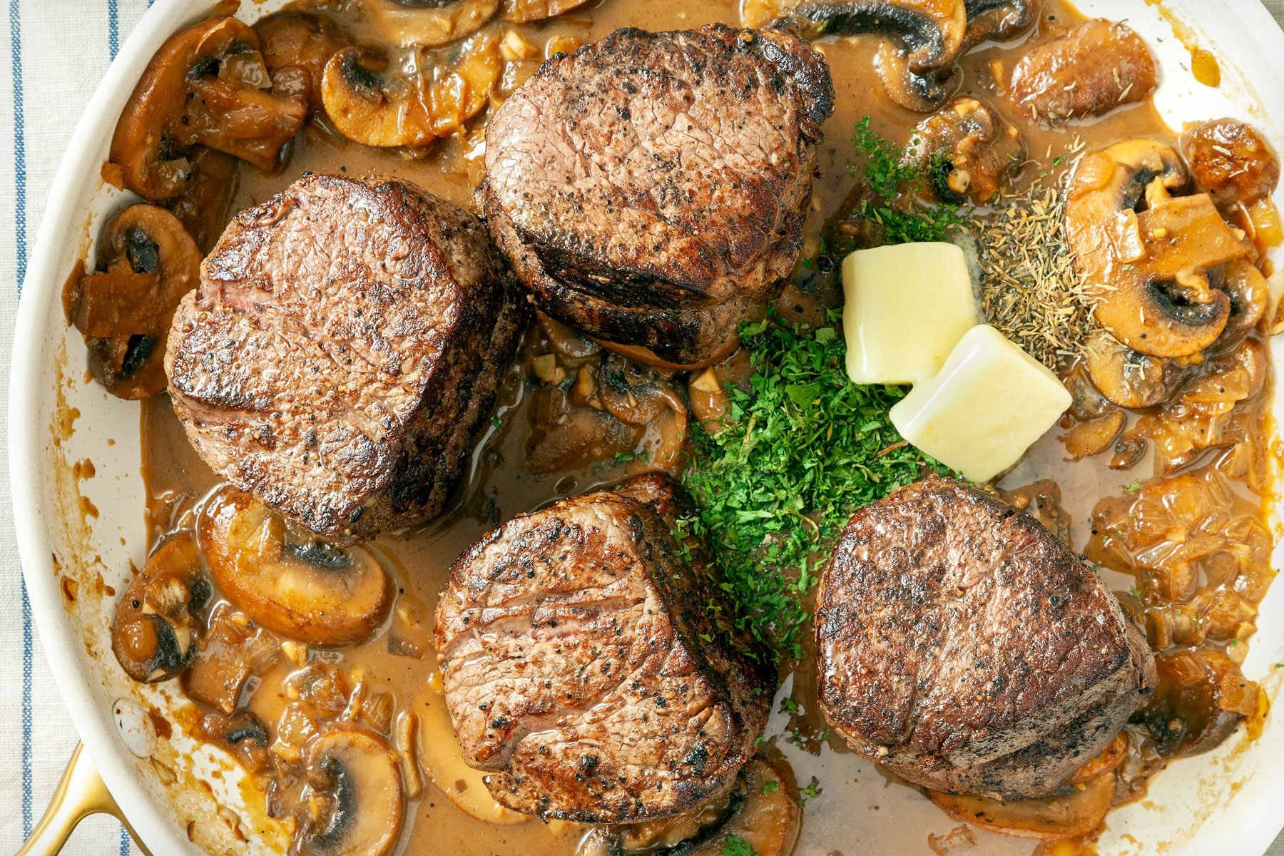 overhead shot; Added butter, parsley, thyme and pepper to mushrooms in pan, Cooking steaks in same pan placed over kitchen towel;