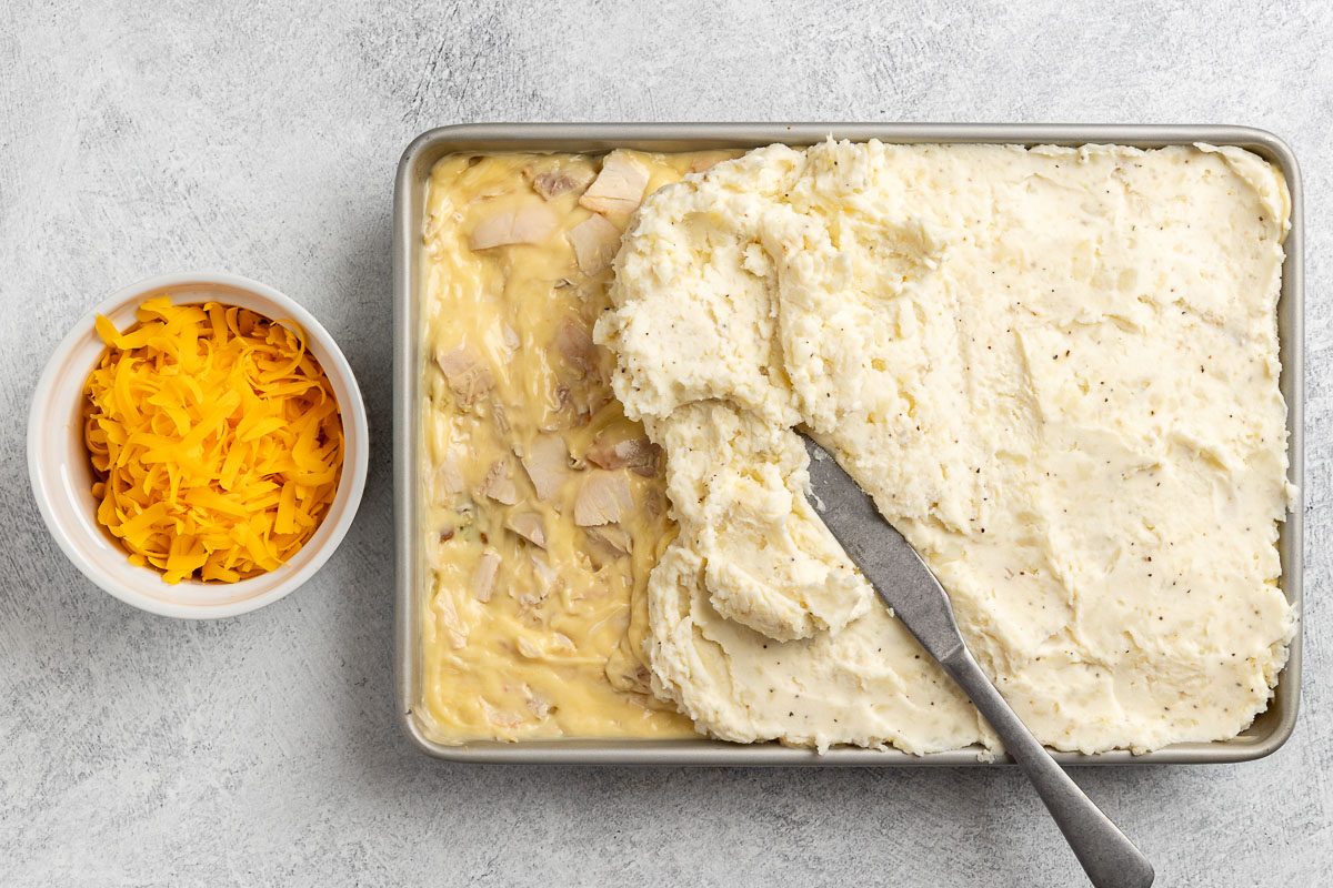 Taste of Home Thanksgiving Casserole recipe photo of the turkey, mashed potatoes, and cheddar cheese added to the top of the stuffing in the baking dish.