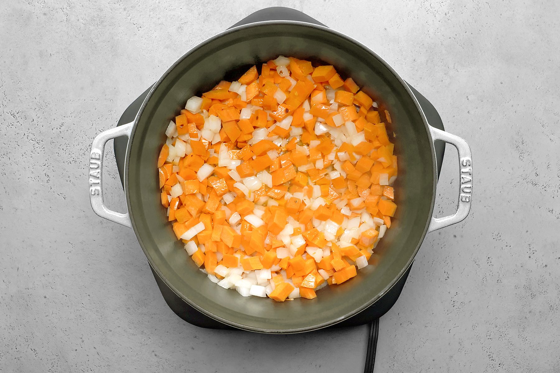 A large pot containing a mix of diced carrots and onions sits on a gray surface.