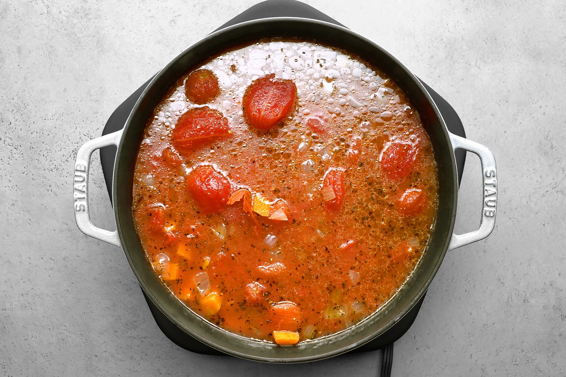 A pot of tomato soup is shown simmering on a stove. 