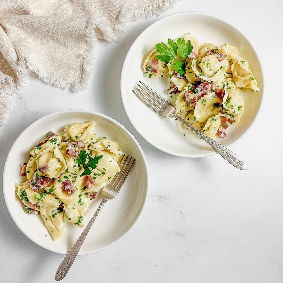 Tortellini Carbonara|Cooked and drained tortellini in a white colander on a marble surface for Taste of Home tortellini carbonara.|Cooked bacon on paper towels on a wooden board on a marble surface for Taste of Home tortellini carbonara.|Taste of Home tortellini carbonara in a white skillet on a marble surface.|Taste of Home tortellini carbonara in white ceramic bowls with a linen napkin on a marble surface.|Taste of Home tortellini carbonara in white ceramic bowls with a linen napkin on a marble surface.