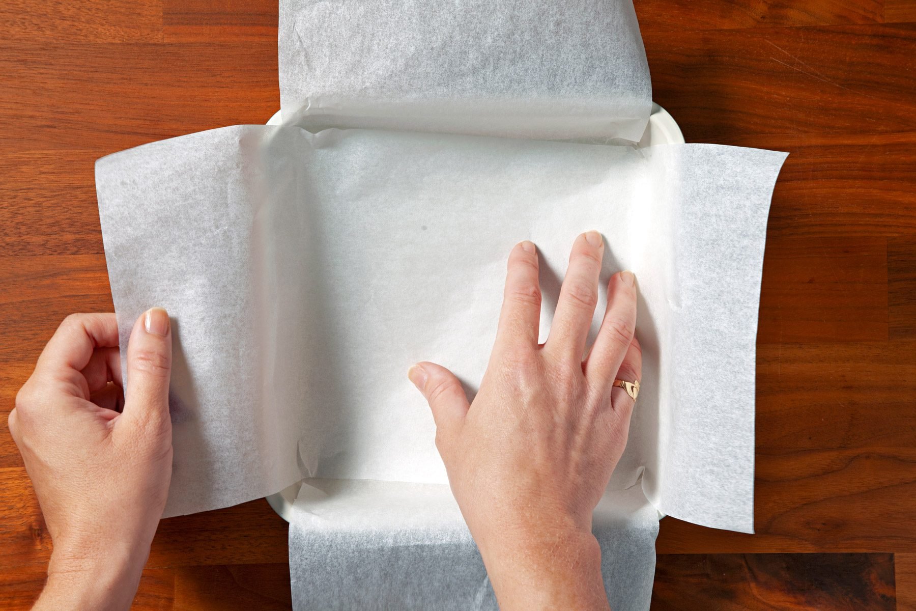 Two pieces of paper fit cross-wise over each other in the pan extend over the edges of the pan. A persons hands can be seen placing the papers.