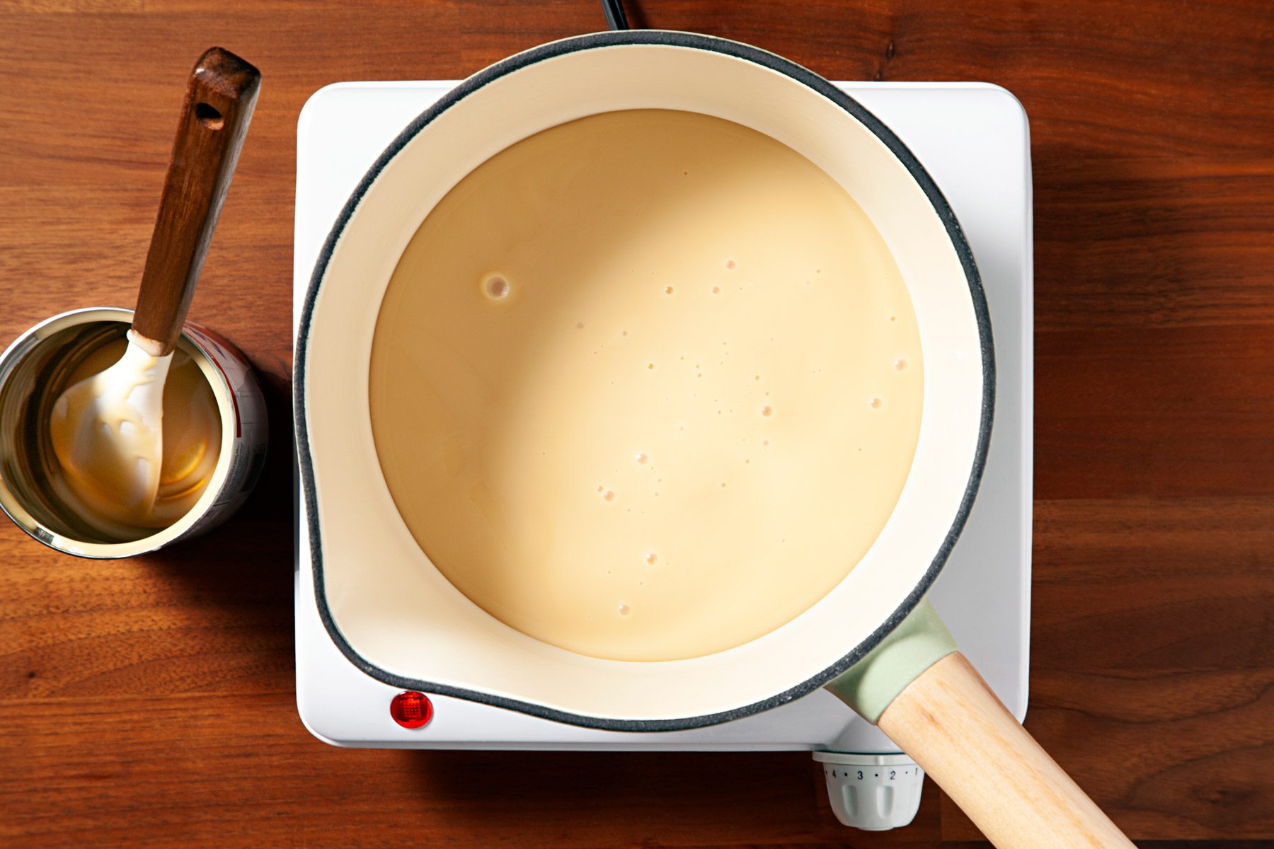 Condensed milk inside a saucepan is being warmed over a stovetop.