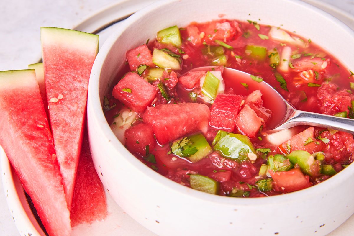 Watermelon gazpacho served in bowl with watermelon wedges on plate