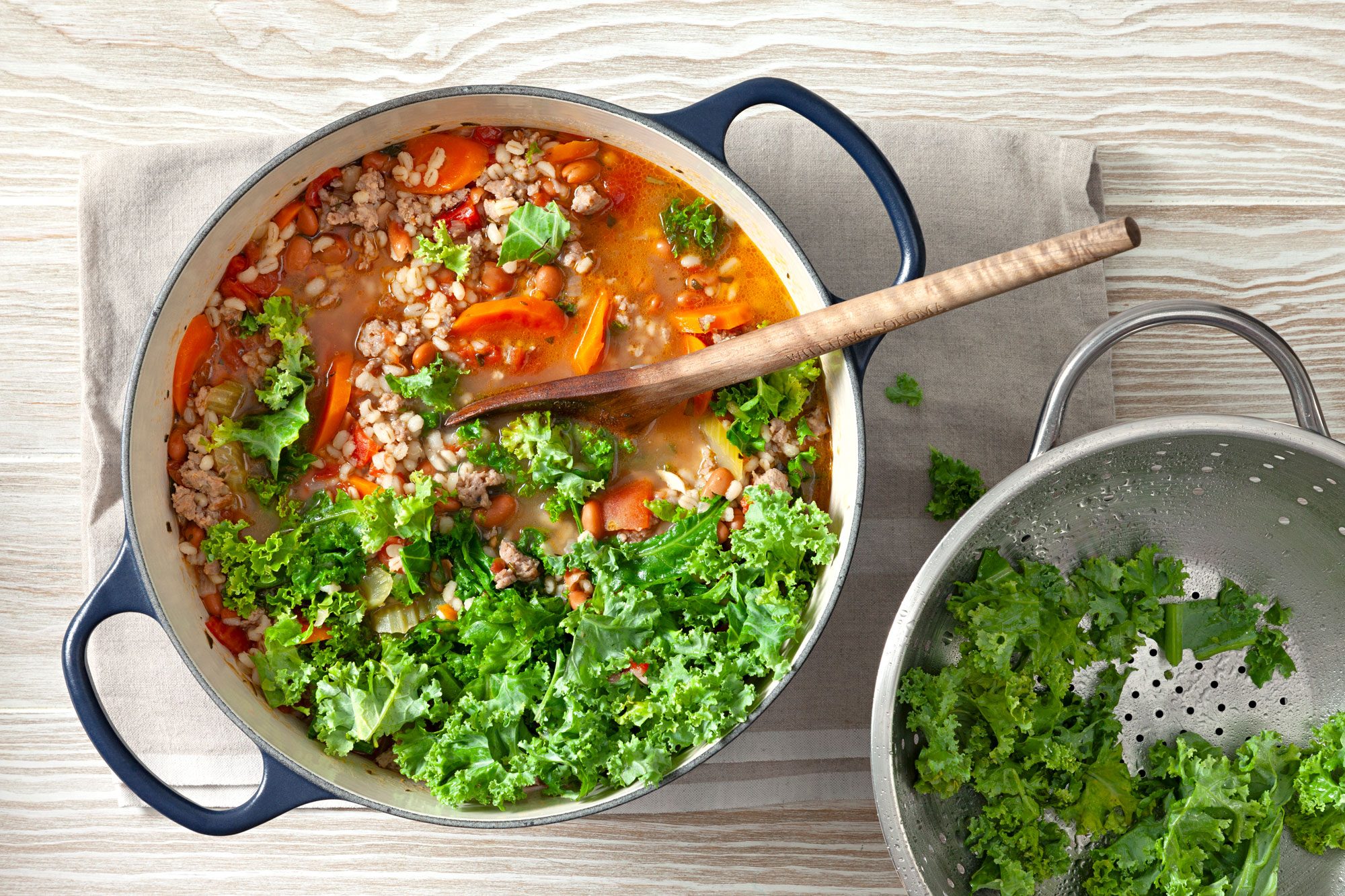 Italian Sausage Bean Soup in a dutch over with long serving spoon and sprinkled chopped fresh kale