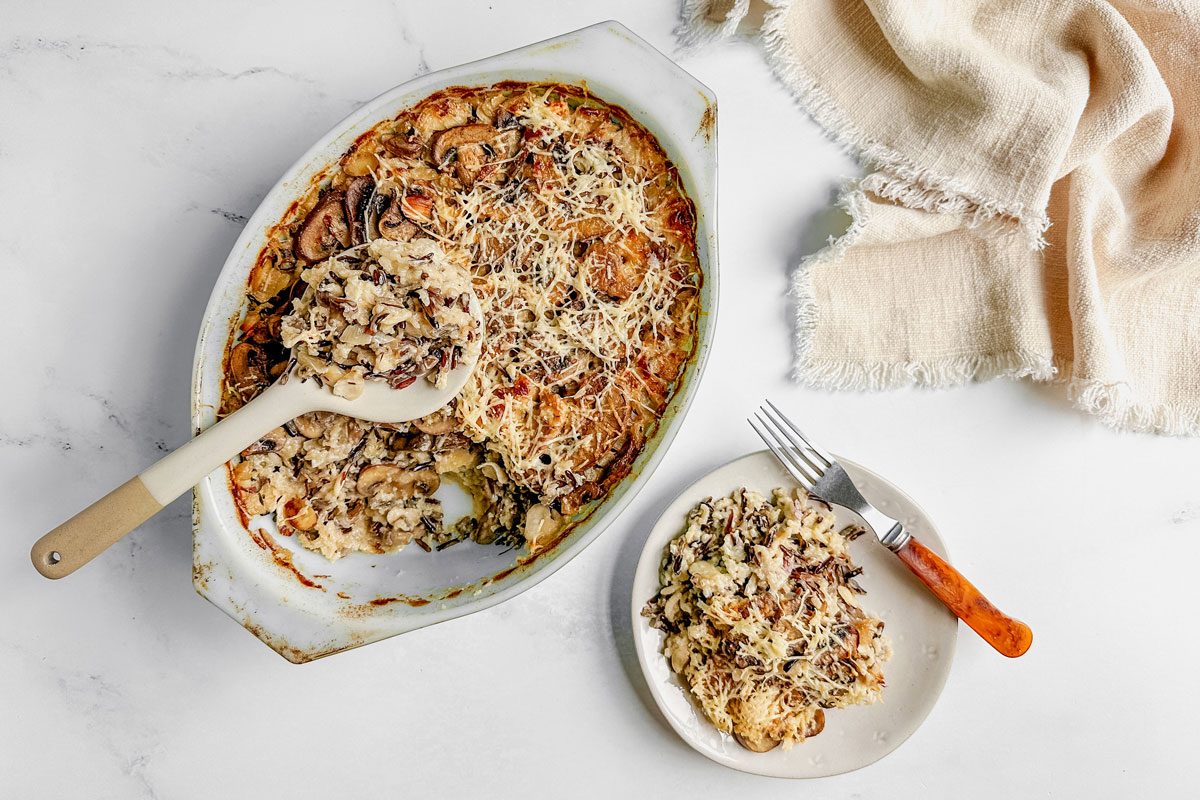 Taste of Home wild rice casserole in a pyrex dish and a ceramic plate next to a linen napkin on a marble surface.