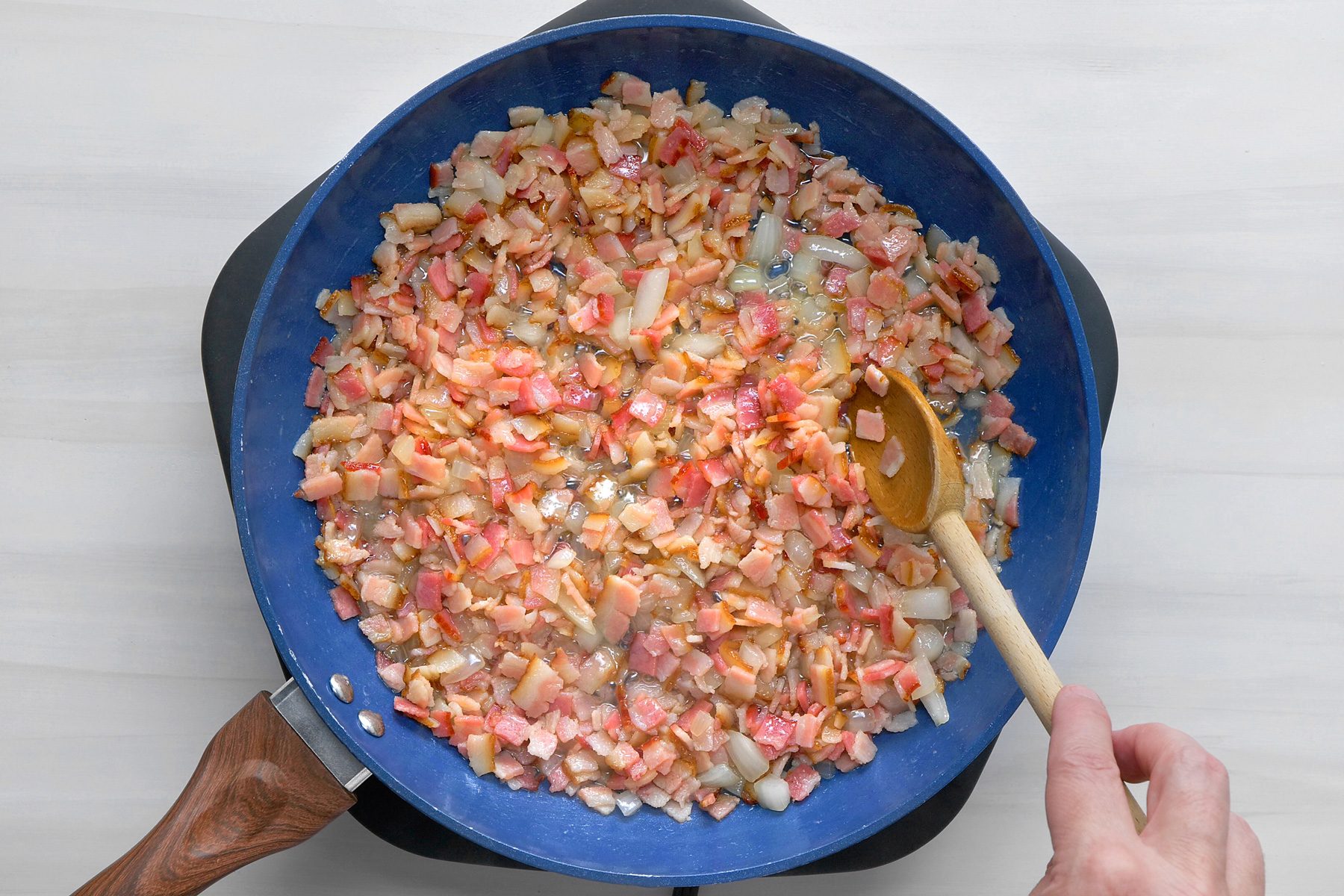 overhead shot; white background; In a large skillet, cooking bacon and onion