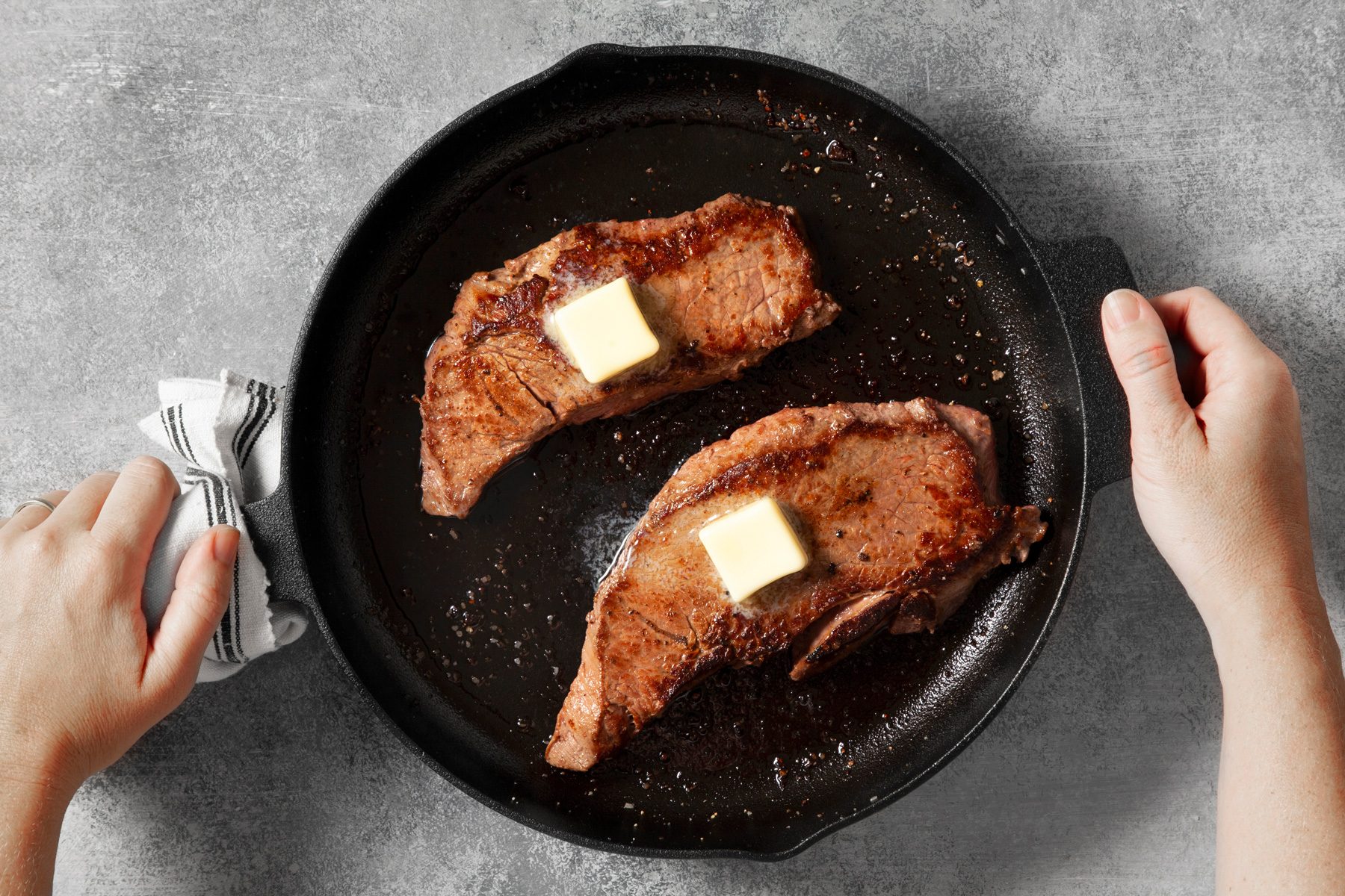 overhead shot; light grey background; Topped each steak with 1 tablespoon butter over cooked steak in a large skillet