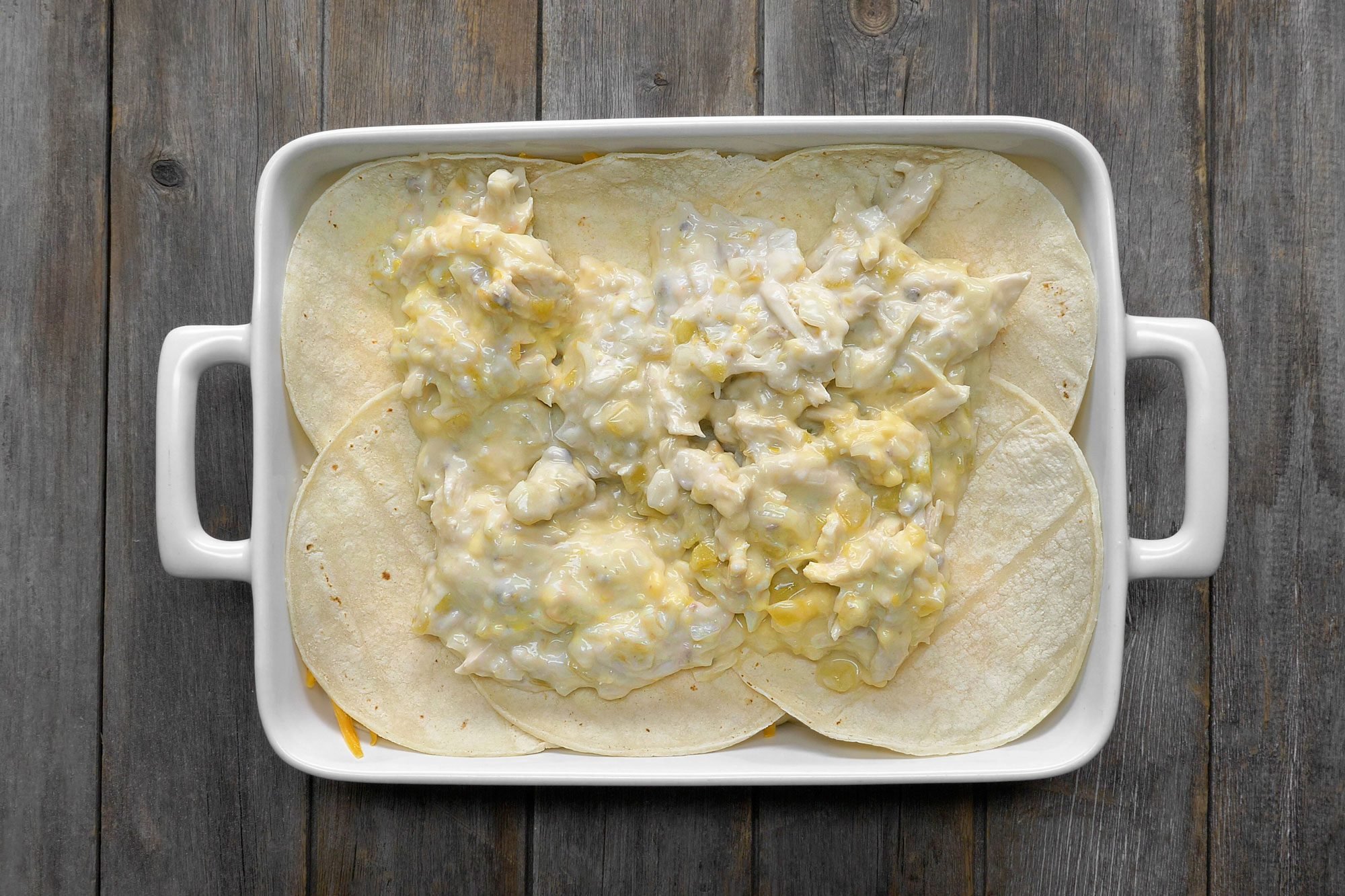 Layer the tortillas topped with chicken mixture in a greased baking dish; wooden background;