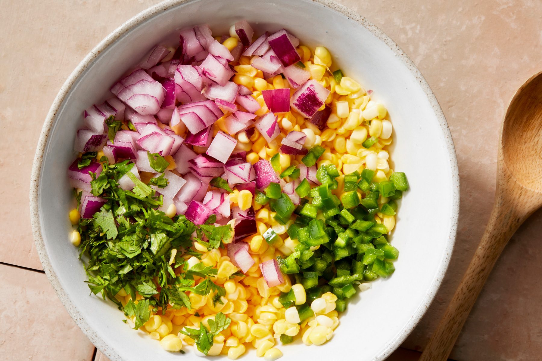 Overhead shot of add red onion; jalapeno; cilantro and lime juice; stir to combine; cover and refrigerate at least 1 hour; wooden spoon; cream square tiles background;