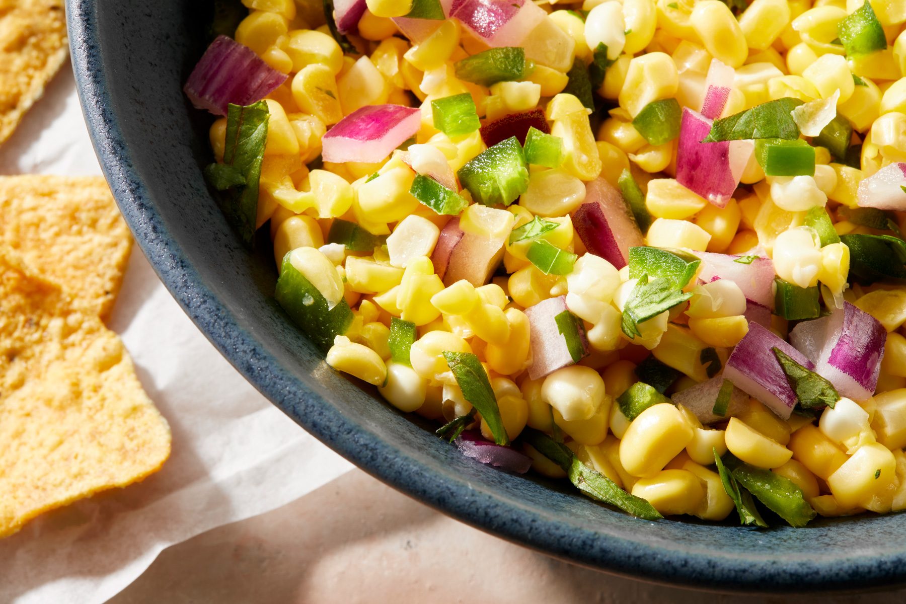 Close shot of Copycat Chipotle Corn Salsa; in a black bowl; serve with fresh corn chips; cream square tiles background