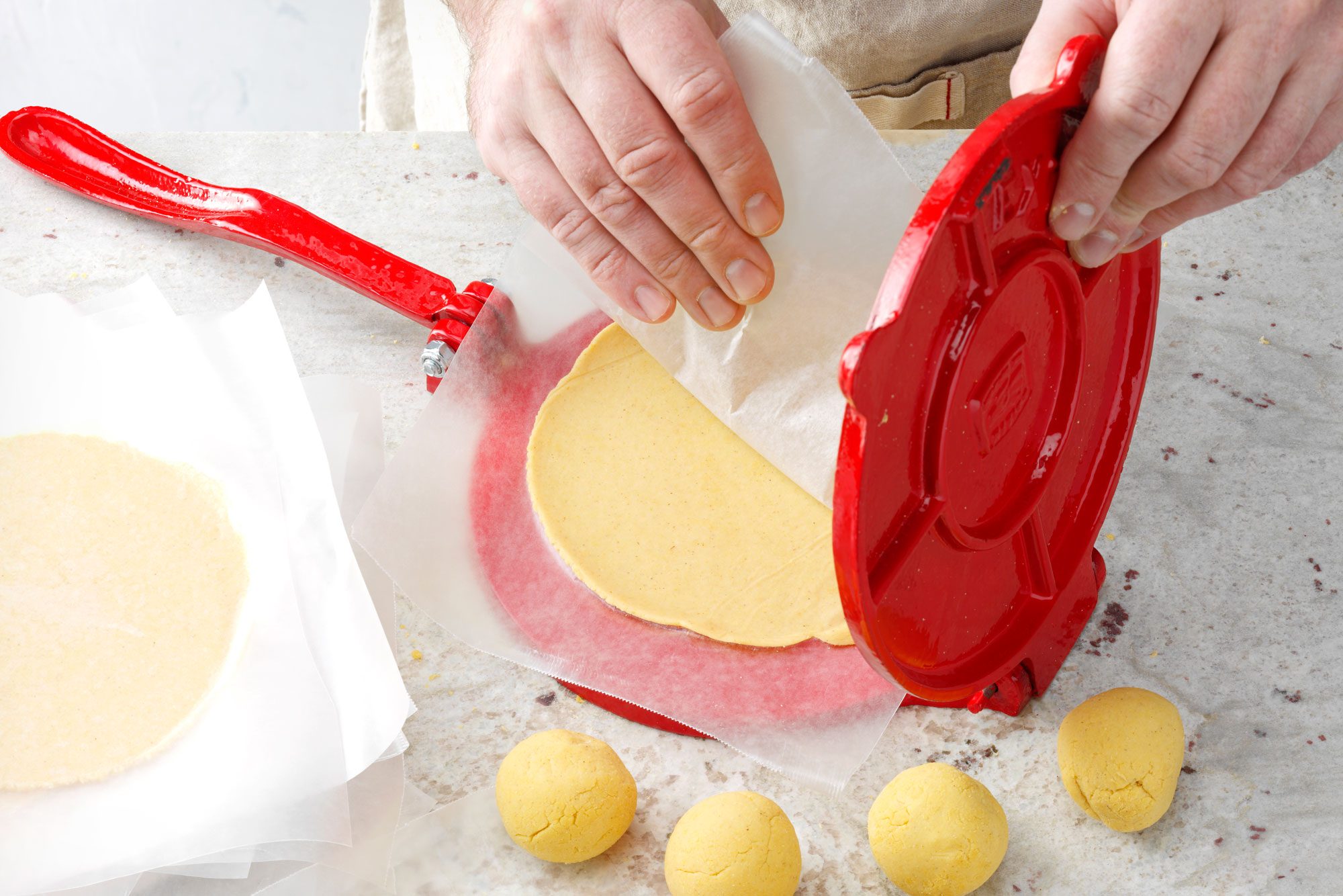 dough ball being flatted between wax paper using a tortilla press