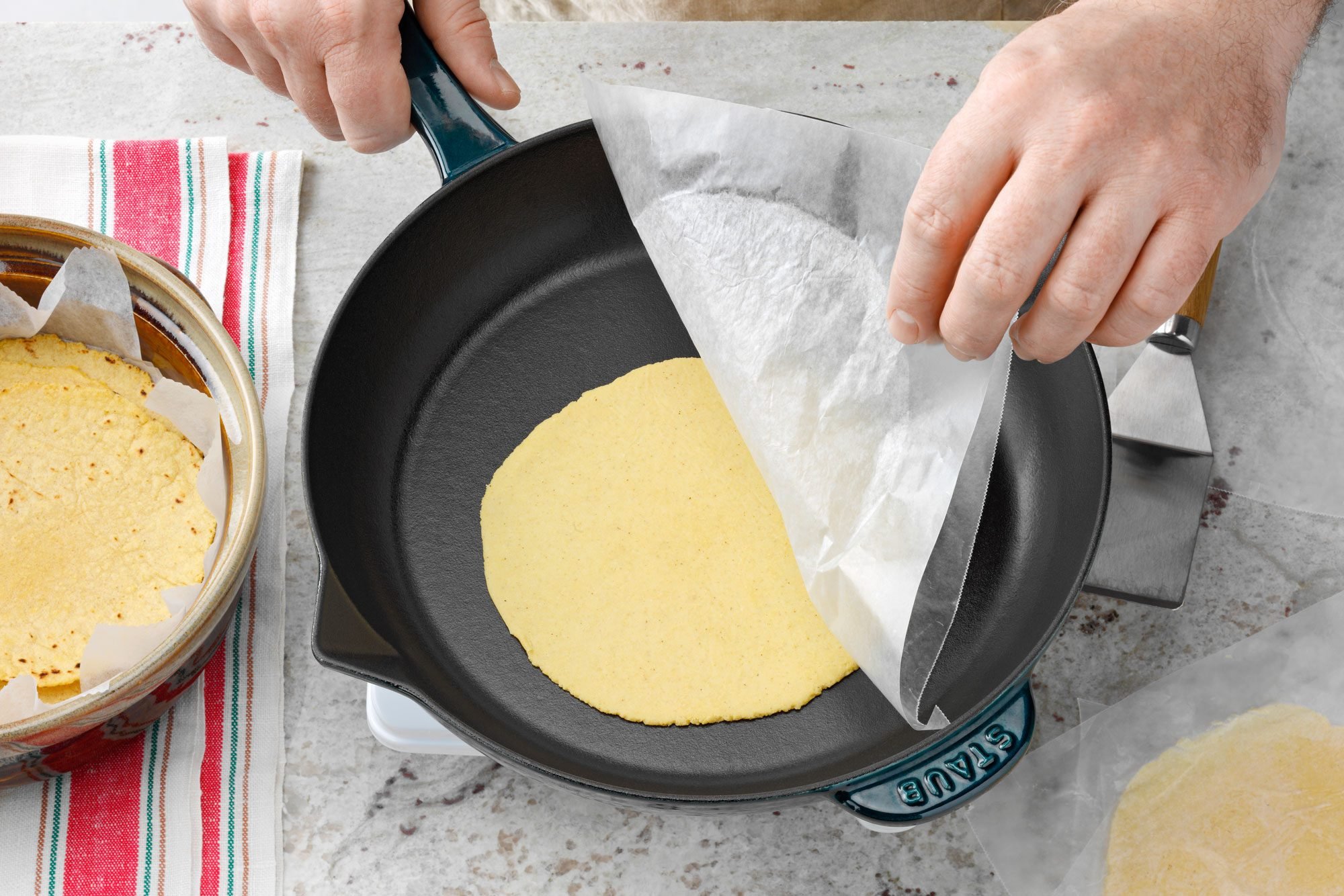 tortilla in skillet with wax paper being actively removed