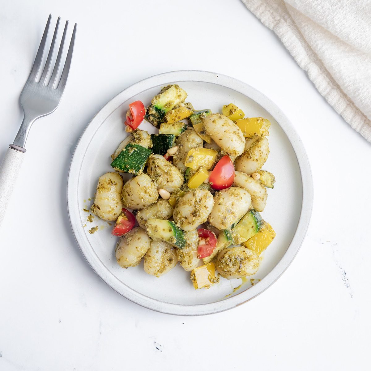 EXPS Overhead Beauty Shot for Taste of Home Pesto Gnocchi with one serving on a white plate on a marble surface.