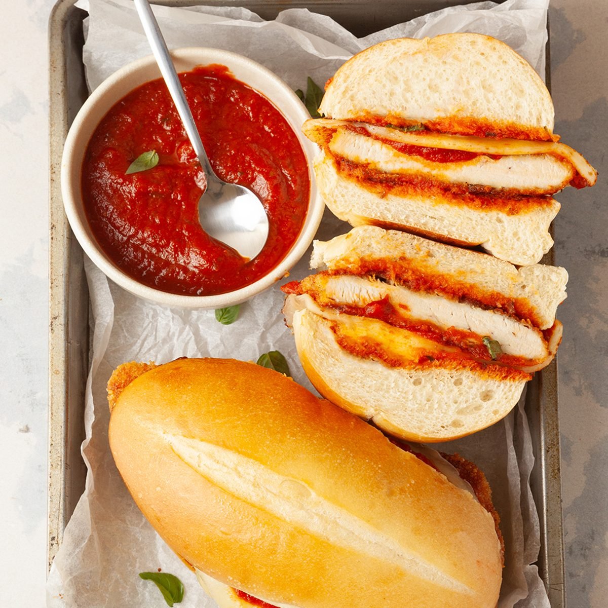 Two Taste of Home Parmesan Chicken Sandwiches with a bowl of marinara sauce on a metal tray