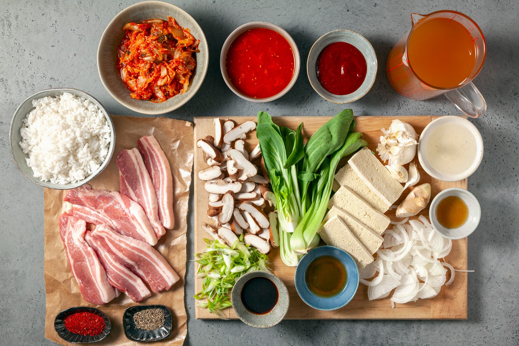 overhead shot; light grey background; Kimchi Soup ingredients placed on a wooden board and parched paper, over background