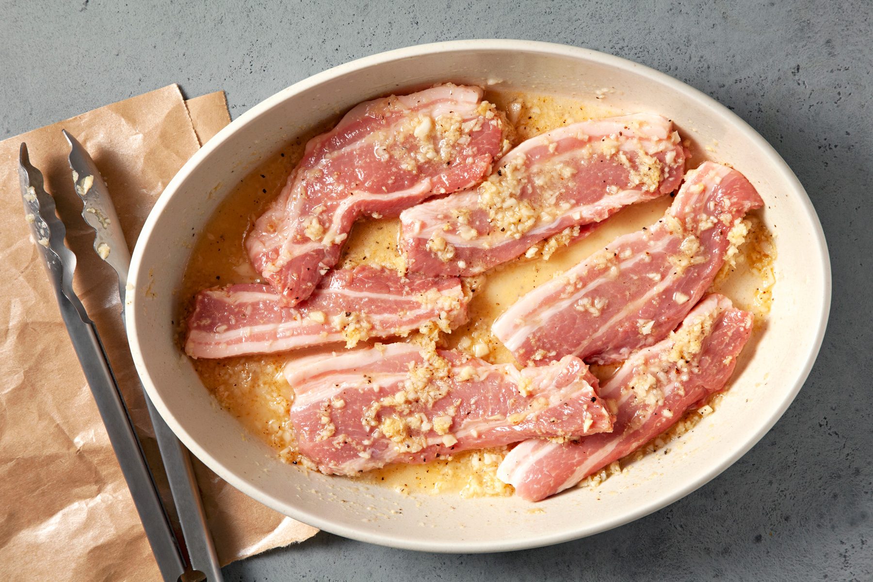 3/4th shot; light grey background; In a shallow dish, combined the first 5 ingredients, Add pork to coat; a tong is placed nearby over a brown paper