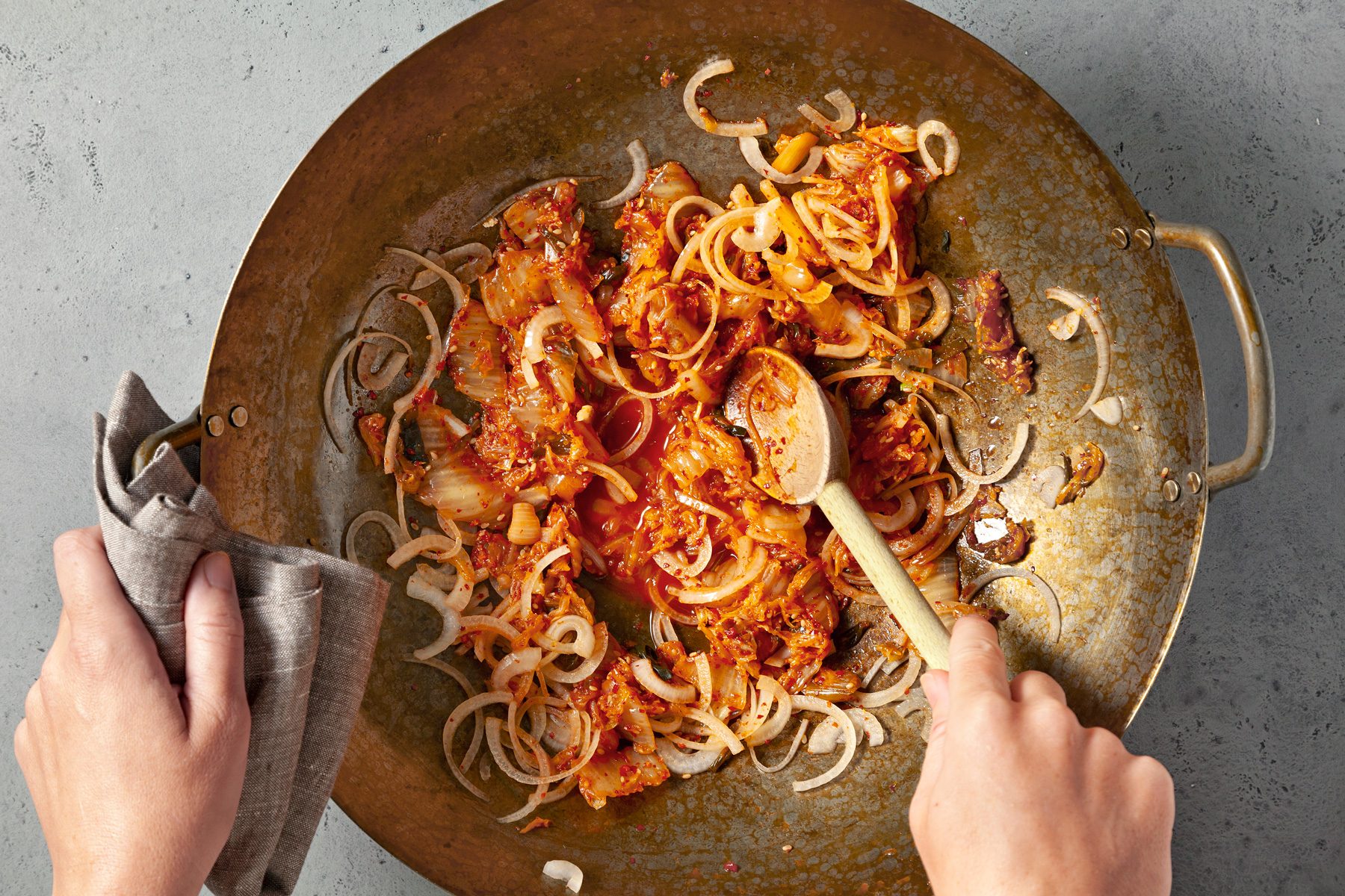 overhead shot; light grey background; In a wok or large saucepan, cooking kimchi over medium heat until tender, Added onion cooking and stiring until onion is tender with a spatula