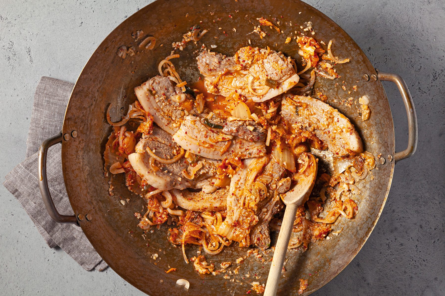 overhead shot; light grey background; in a same wok, pork is added