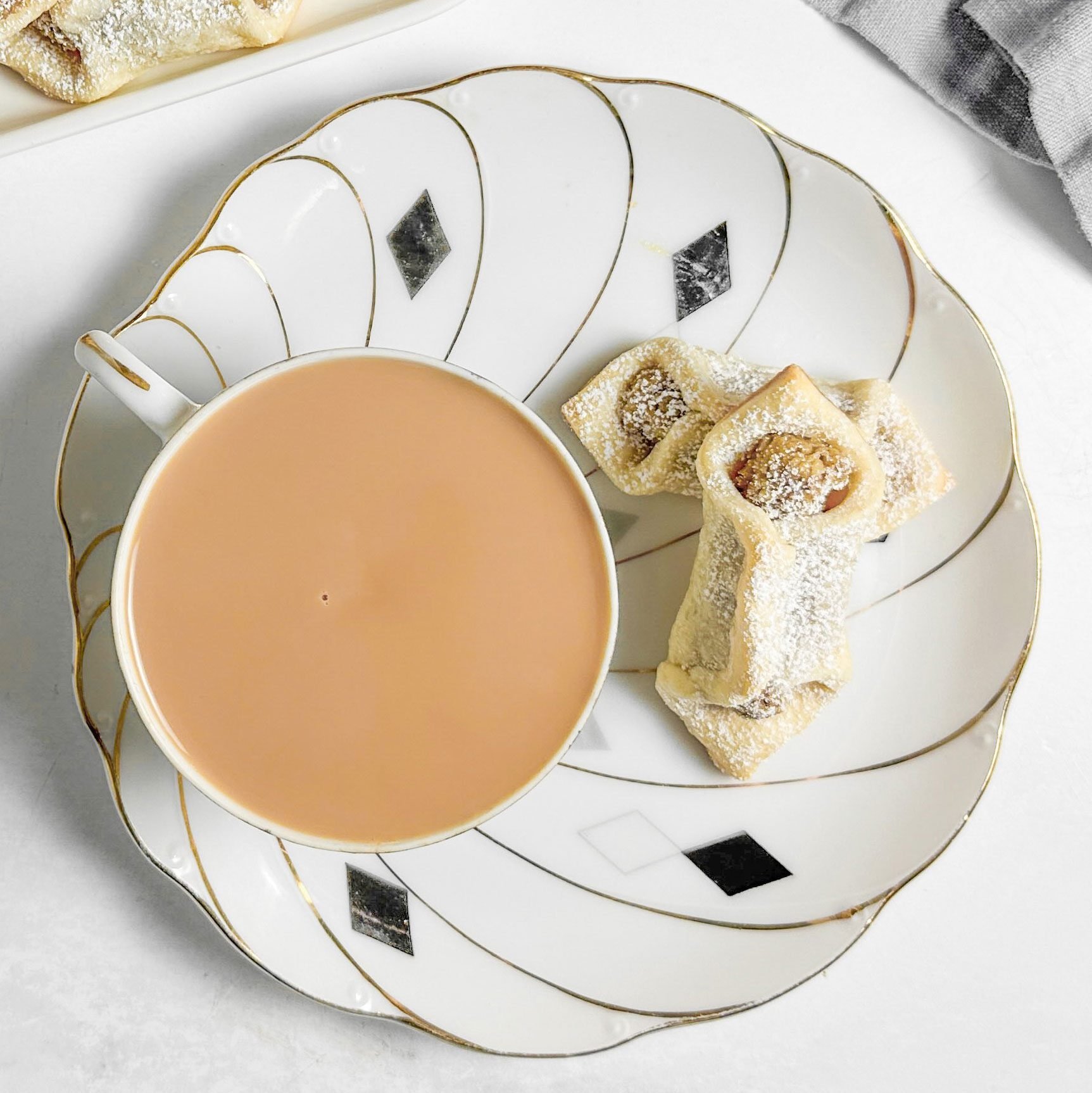 Taste of Home Kolacky Cookies on a white tray next to a cup of tea on a marble surface