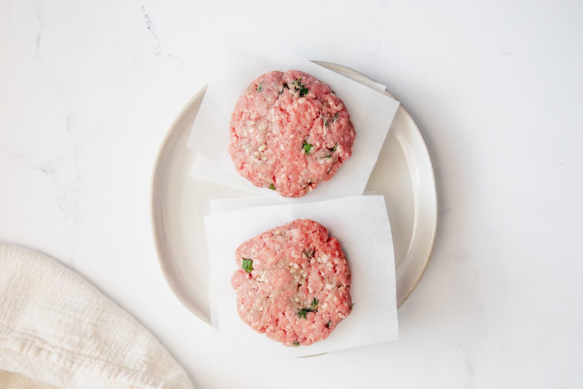 Overhead shot for Taste of Home Lamb Burgers, uncooked burgers on a plate with mint and fresh thyme.