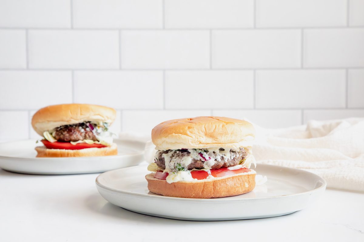 Close up image for Taste of Home Lamb Burgers, two burgers cooked and being served with toppings on a plate.