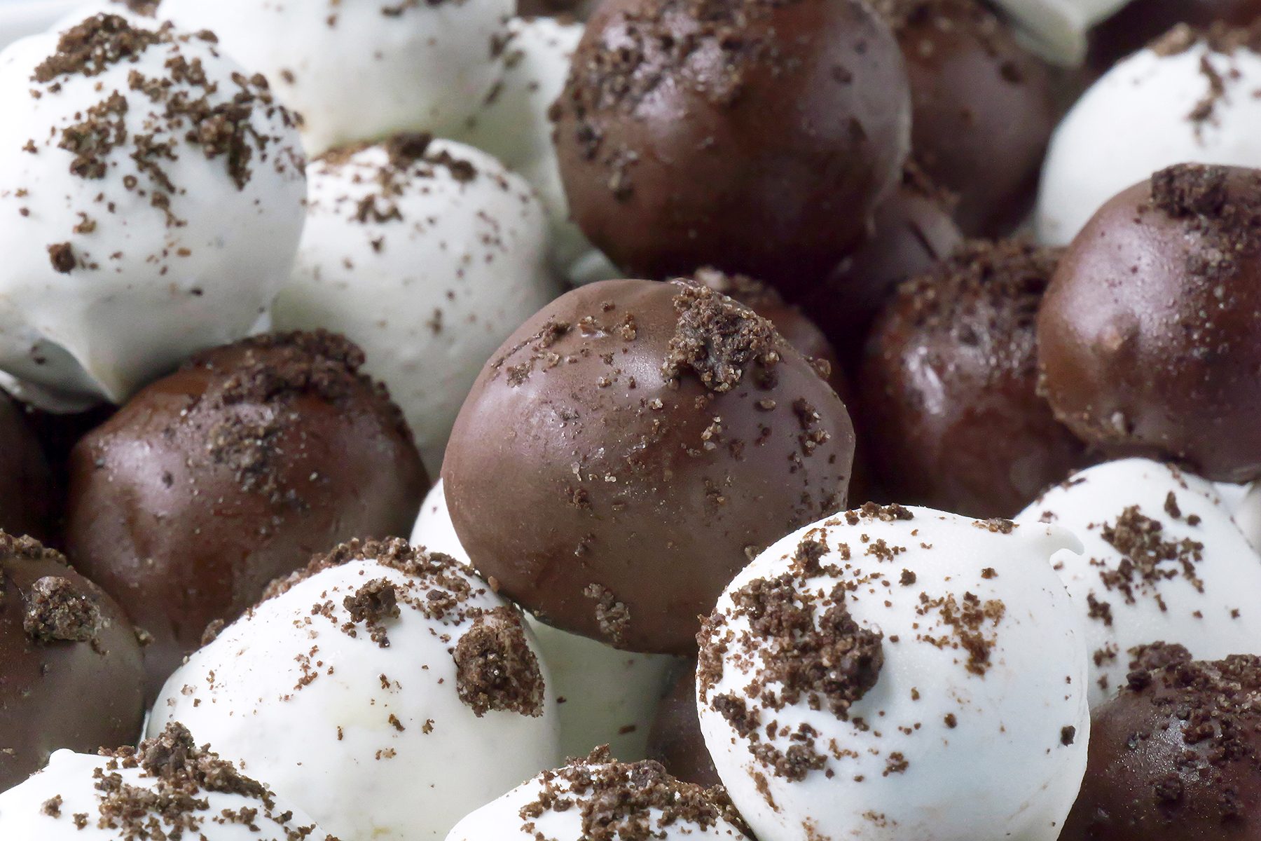 A close-up view of chocolate truffles, some coated in white chocolate and others in dark chocolate. The truffles are sprinkled with bits of crushed cookies, giving them a textured appearance.