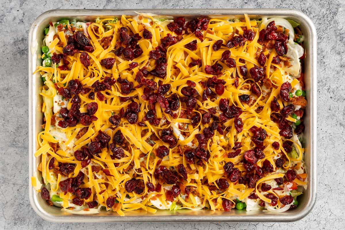 Taste Recipes Overnight Salad photo of the layers topped with the dressing, cheese, bacon, and dried cranberries.