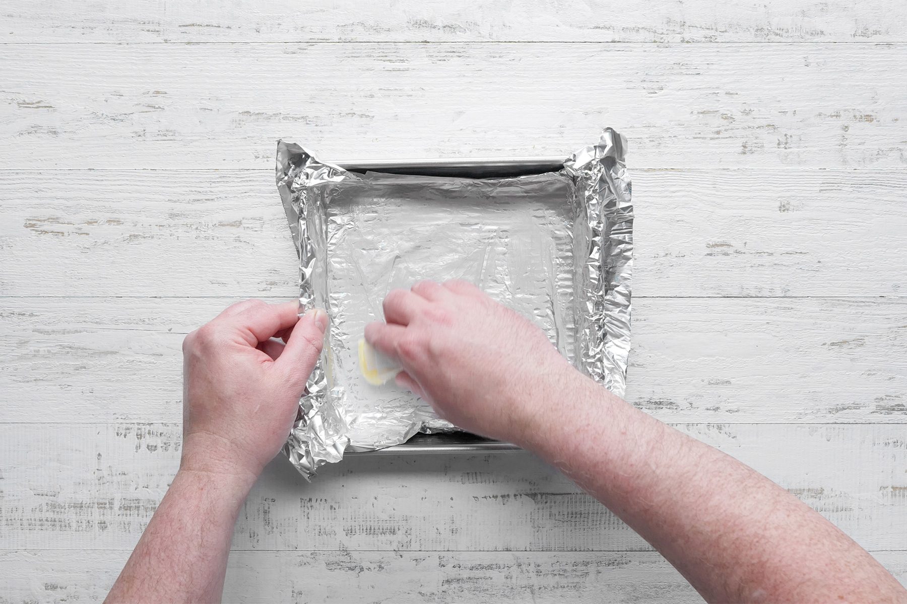 Overhead shot of line square pan with foil; greased with butter; white wooden background;