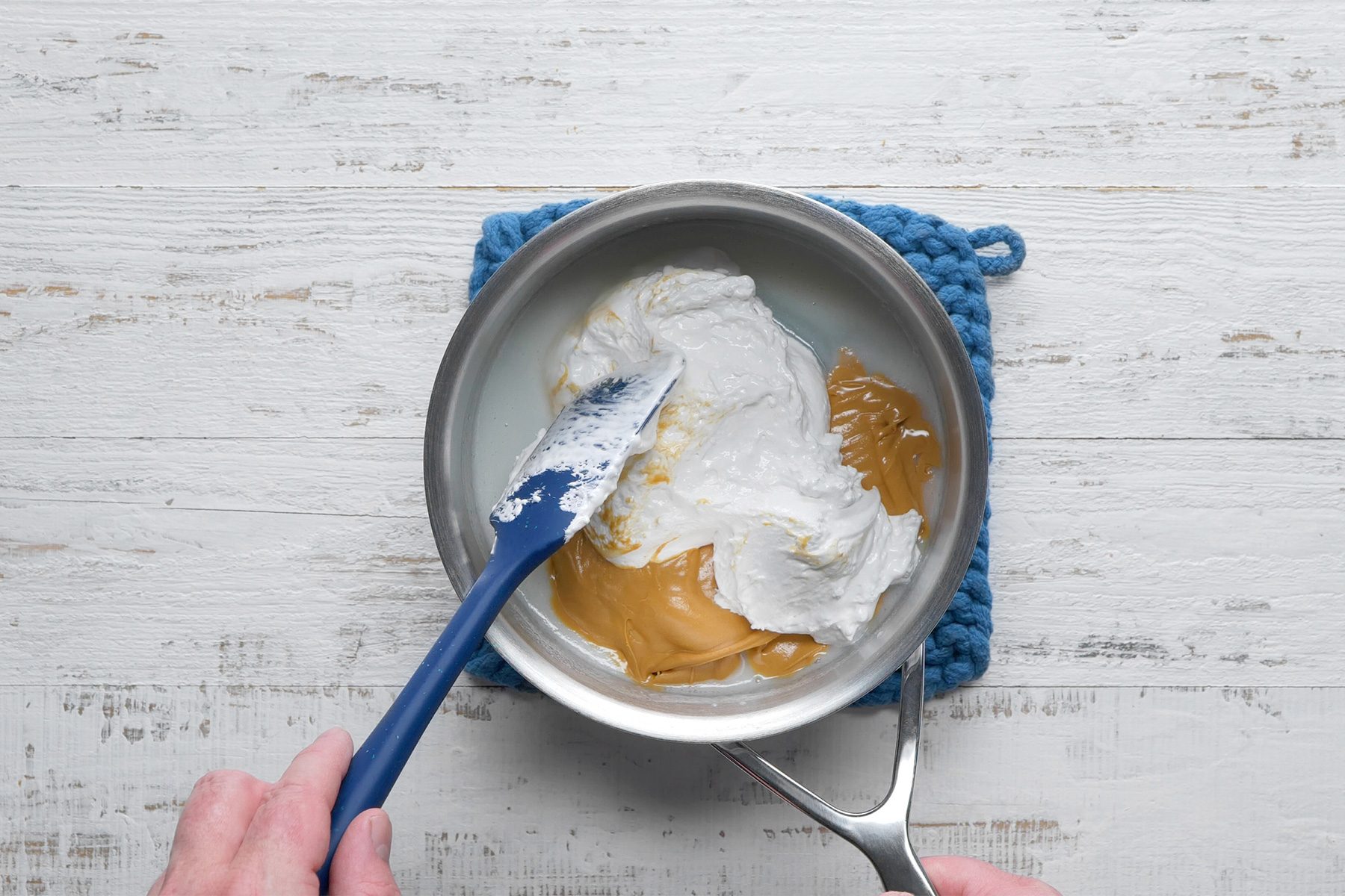 Overhead shot of stir in peanut butter and marshmallow creme until blended; spatula; heavy saucepan; white wooden background;