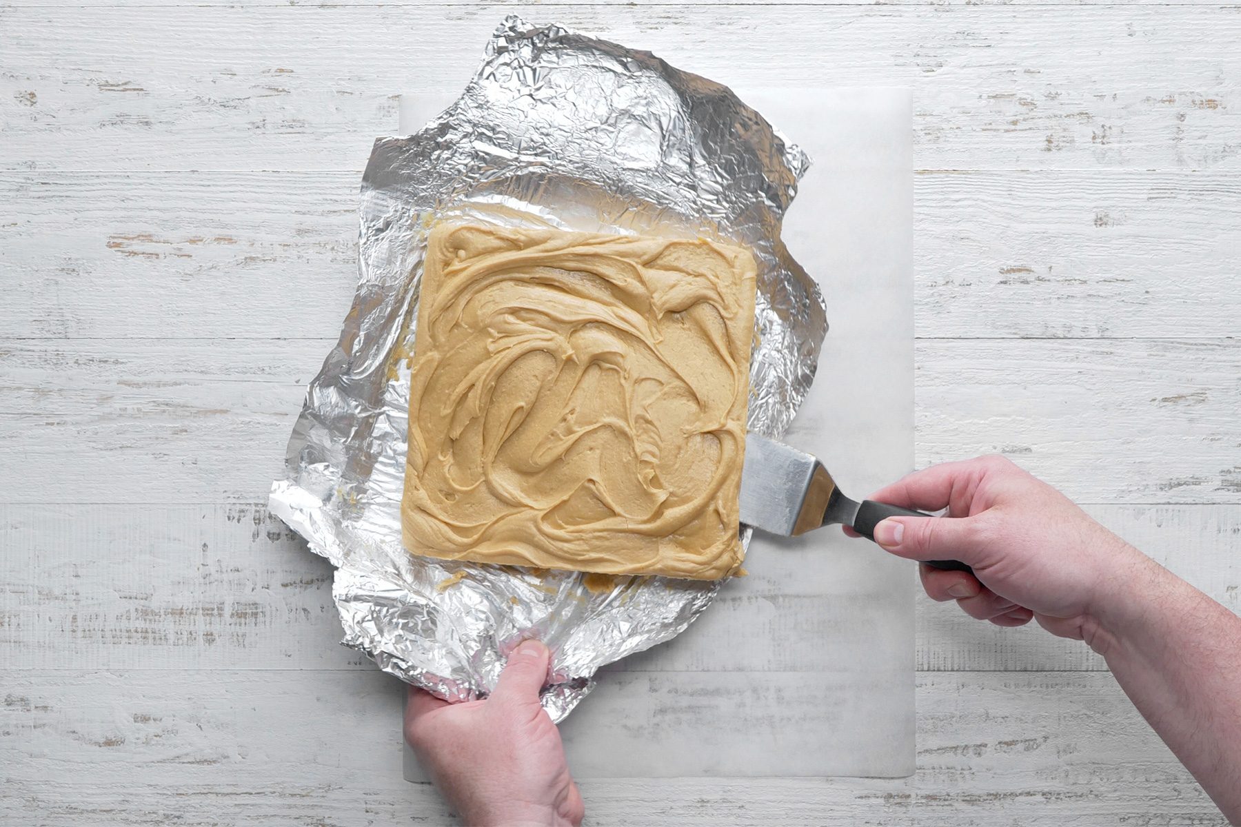 Overhead shot of lift fudge out of pan; flat spatula; white wooden background;