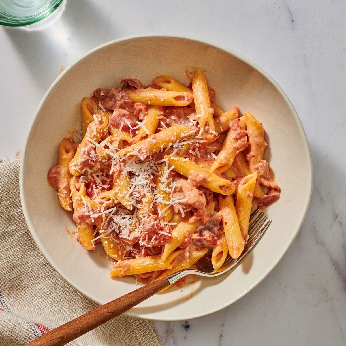 A bowl of pasta alla vodka with Parmesan on the side and a fork in the bowl