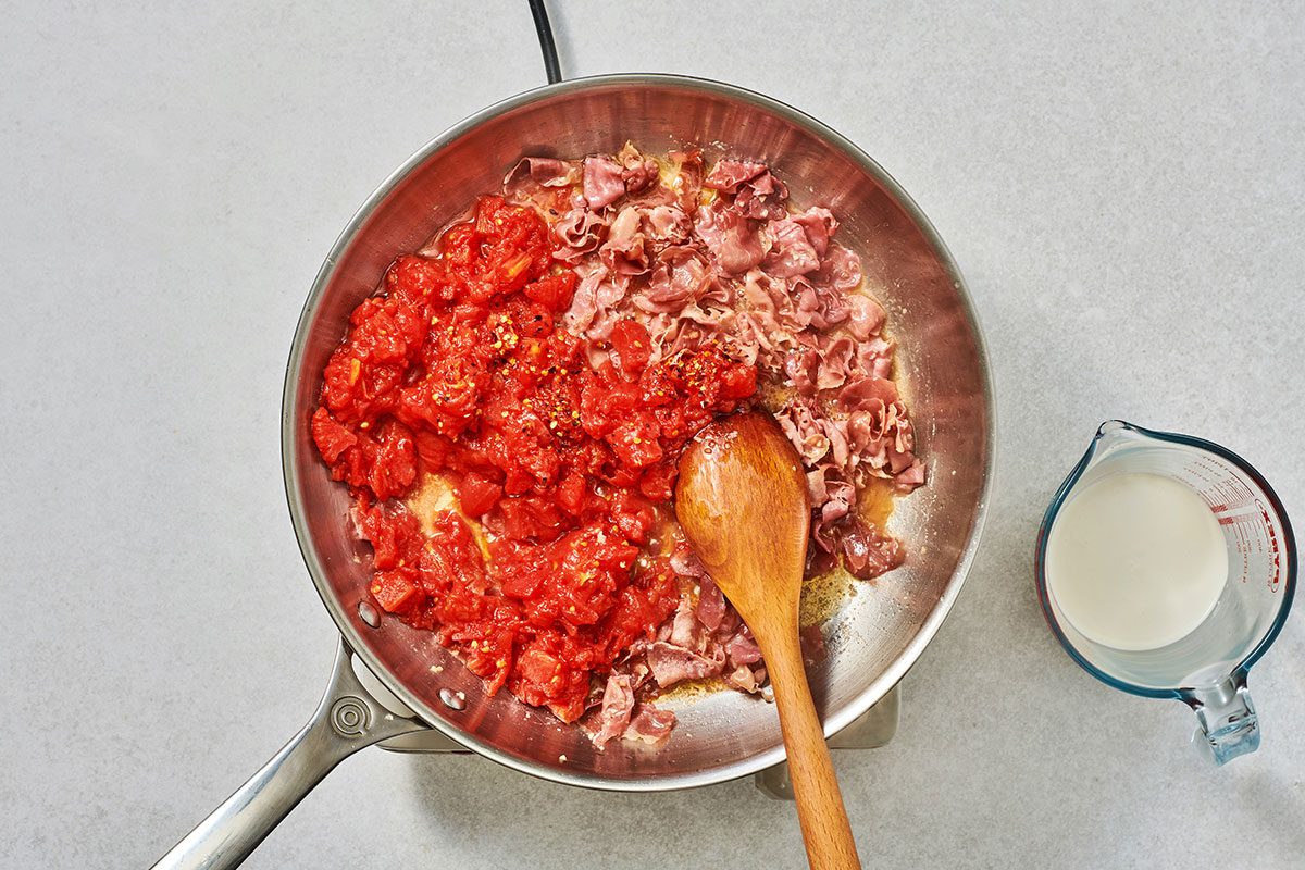 Cooking prosciutto with tomatoes garlic vodka and red pepper flakes in the skillet to prepare vodka sauce