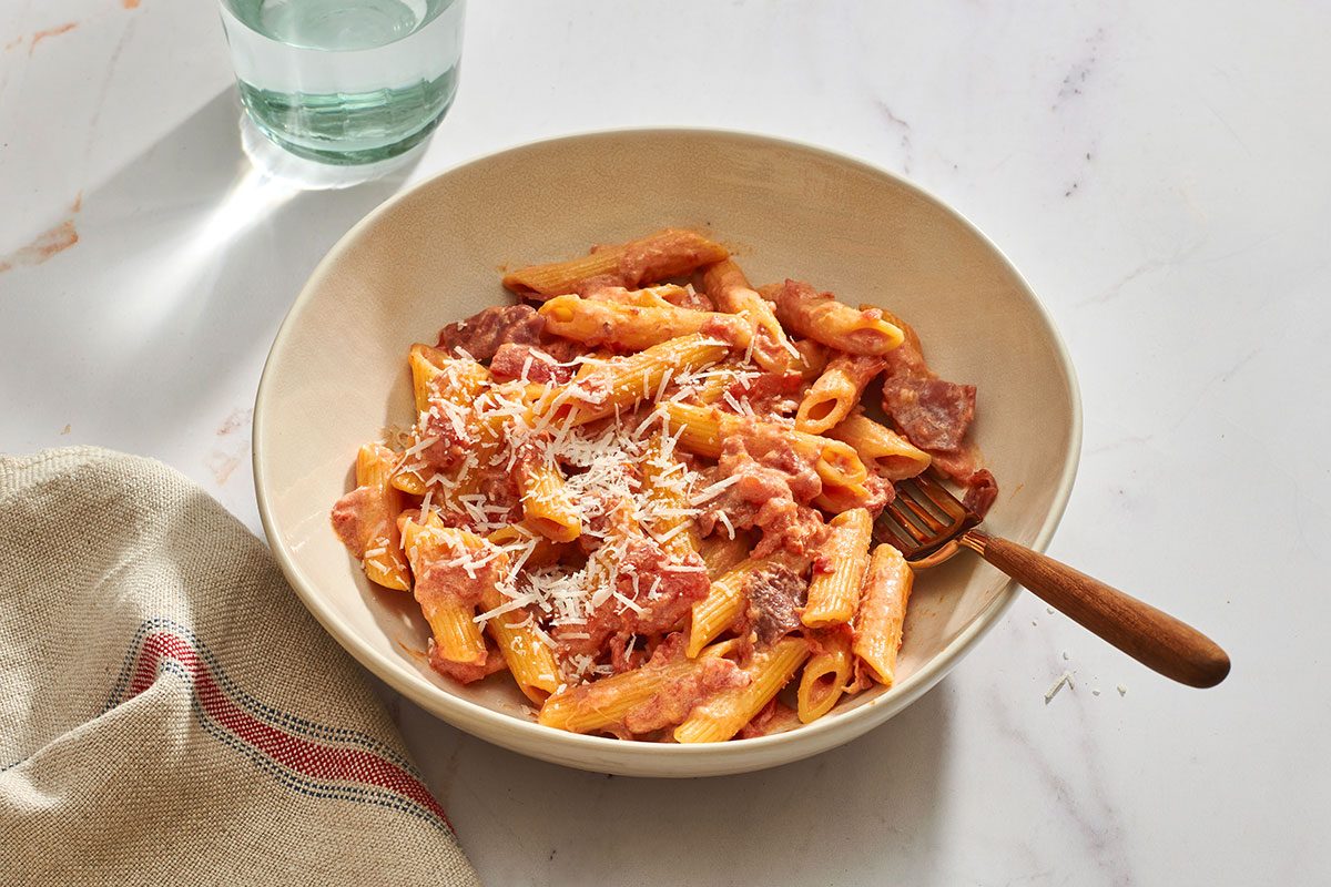 A bowl of pasta alla vodka with Parmesan on the side and a fork in the bowl