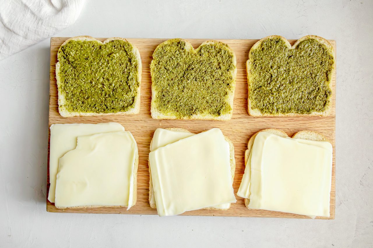 Overhead shot for Taste of Home Pesto Grilled Cheese, sandwiches being assembled on a wooden cutting board.