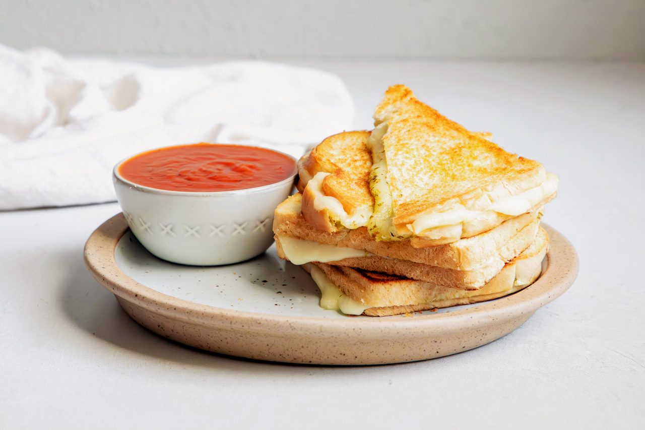 Beauty Shot for Taste of Home Pesto Grilled Cheese with sandwich on a plate served alongside warmed pizza sauce.