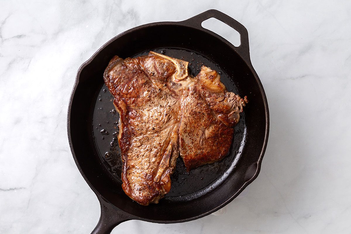 Steak seared in heated oil in a cast iron skillet for step two of Porterhouse Steak recipe for Taste of Home