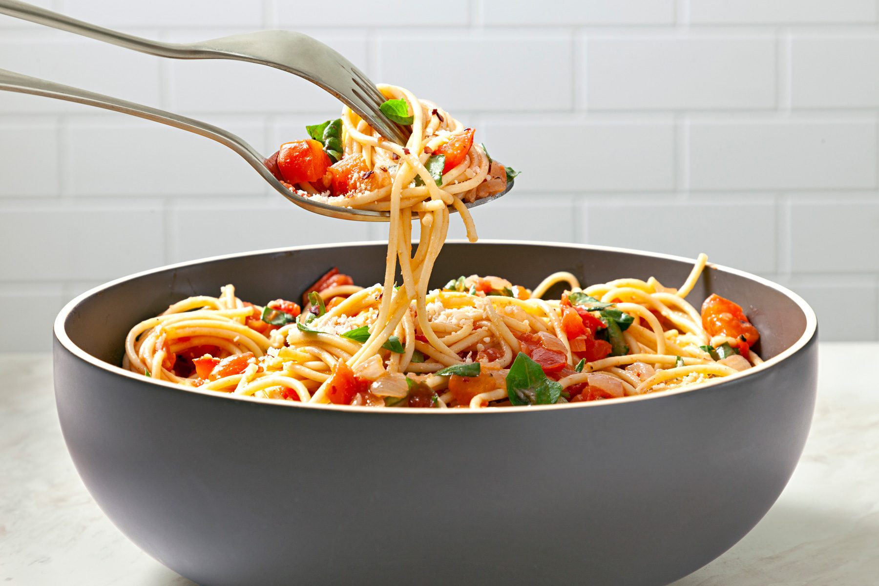 Table view shot of Spaghetti Pomodoro; serve with Parmesan cheese; and top with additional fresh basil and crushed red pepper flakes; fork; spoon; marble surface