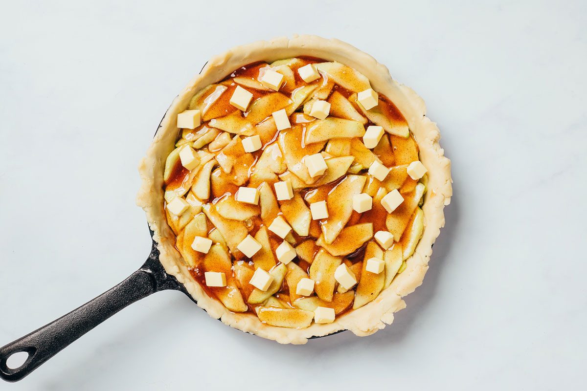 Adding the apple filling with caramel and cubed butter to the crust of the Cinnamon Apple Pie recipe by Taste of Home