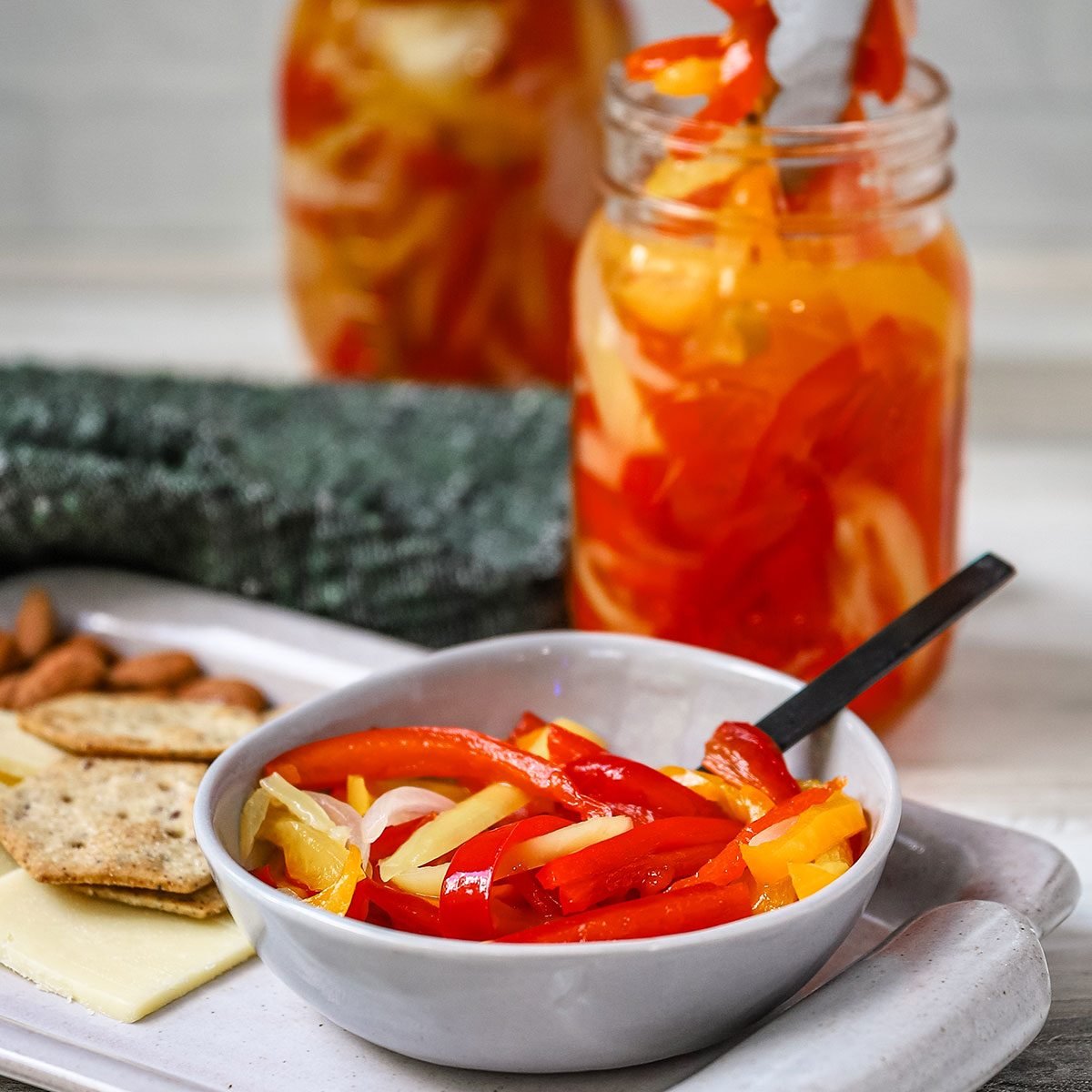 Homemade sweet pickled peppers are served as a snack with cheese, crackers, and almonds.