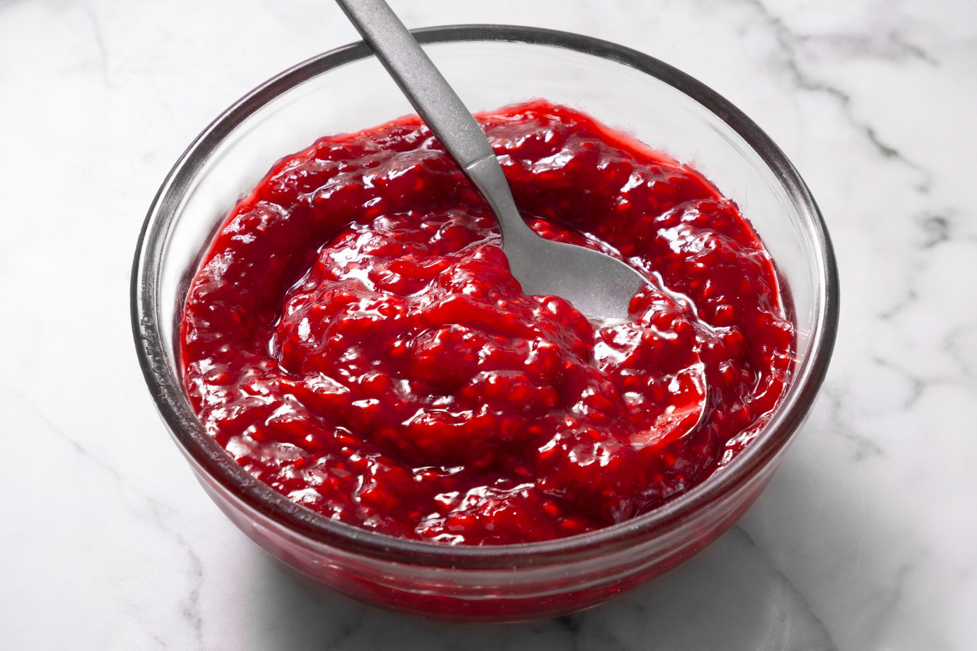 A glass bowl filled with a vibrant red raspberry jam